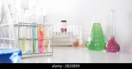 Foto von Laborglas, die farbige Flüssigkeiten enthalten, während sie auf einem weißen Tisch, der über weißem Hintergrund isoliert ist, zusammengefügt werden. Stockfoto