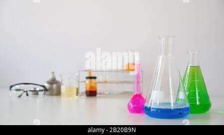 Foto von Laborglas mit farbigen Flüssigkeiten und Schutzbrillen, während sie auf weißem Tisch über isoliertem weißem Hintergrund zusammengefügt werden. Scie Stockfoto