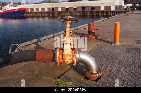 Nahansicht einer großen Wasserleitung und Hahn, der in das Deck am Hafen von Lochinver, Schottland und ein Hochseefischschiff befestigt ist Stockfoto