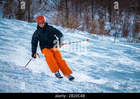 Junger männlicher Skifahrer, der an sonnigen Tagen einen Hang hinuntergeht Stockfoto