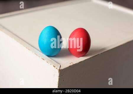 Zwei Collour-Ostereier - blau und rot, auf einer alten weißen Holzkiste Stockfoto