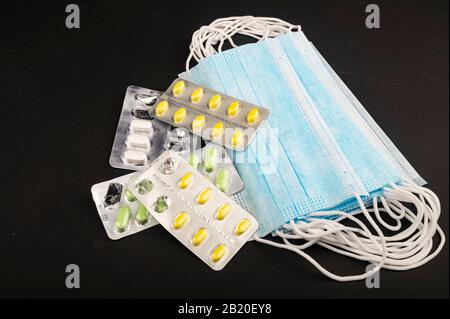 Medizinische Einwegmasken und mehrere Pillenpakete auf schwarzem Hintergrund. Persönliche Schutzausrüstung. Nahaufnahme Stockfoto
