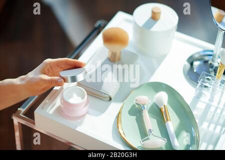 In der Nähe der Hausfrau, die am sonnigen Wintertag einen Kosmetikbecher mit Toilettenartikeln im Wohnzimmer öffnet. Stockfoto