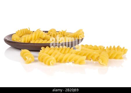Viele ganze ungekochte gelbe Nudelfusilli mit brauner Keramikcoaster isoliert auf weißem Hintergrund Stockfoto
