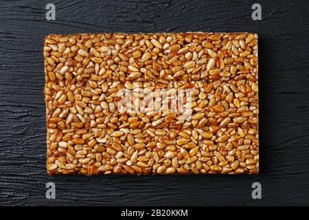 Kachelkozinaki aus Sonnenblumensamen auf schwarzem texturalem Hintergrund. Köstliche orientalische Süßigkeiten Gozinaki aus Sonnenblumensamen, Sesamsamen und Erdnüssen, Stockfoto