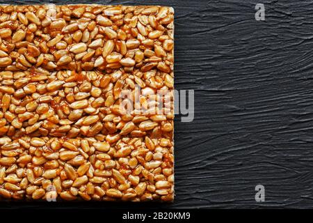 Kachelkozinaki aus Sonnenblumensamen auf schwarzem texturalem Hintergrund. Köstliche orientalische Süßigkeiten Gozinaki aus Sonnenblumensamen, Sesamsamen und Erdnüssen, Stockfoto