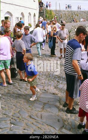 Menschen auf den gepflasterten Straßen von Clovelly im Stadtteil Torridge in Nord-Devon, das in der Fußgängerzone liegt und Kopfsteinpflaster hat. Stockfoto