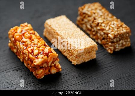 Getreideriegel mit Erdnüssen, Sesam und Sonnenblumenkerne auf einem Schneidebrett auf einem dunklen Steintisch. Ansicht von oben. Die Granola-Bar ist ein schleichender und ein s Stockfoto
