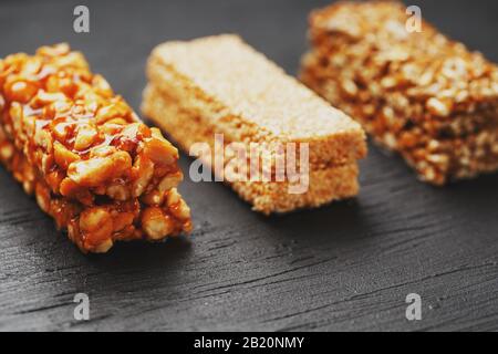 Gesunde Snacks. Fitness Diätkost. Körnerguss mit Erdnüssen, Sesam und Samen auf einem Schneidebrett auf einem dunklen Tisch, Energiestäben. Schwarzer Hintergrund in der Draufsicht Stockfoto