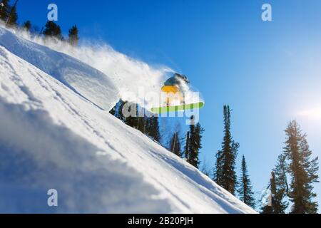 Ein Snowboarder springt an einem sonnigen Tag von einem Sprungbrett in die Hochgebirge. Sonnenstrahlen, weißer Schnee und klares Wetter, blauer Himmel. Stockfoto