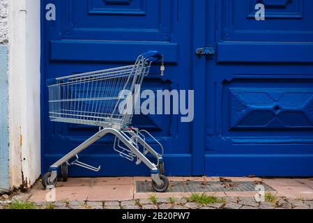 Vor einer großen blauen Eingangstür steht ein leerer Warenkorb Stockfoto