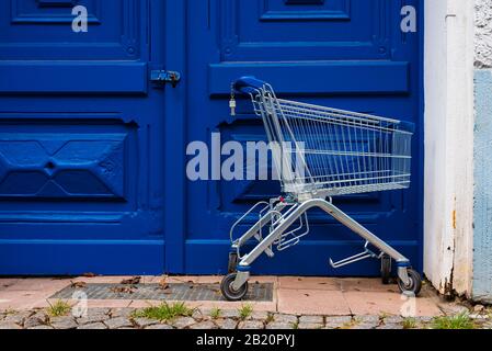 Vor einer großen blauen Eingangstür steht ein leerer Warenkorb Stockfoto