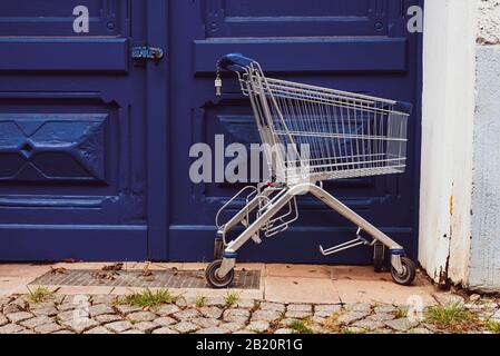 Vor einer großen blauen Eingangstür steht ein leerer Warenkorb Stockfoto
