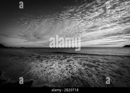 Gegensätzliche Muster von Wolken am Himmel und Rückwäsche von Wellen auf Sand am Mount Maunganui Main Beach, Tauranga Neuseeland. Stockfoto