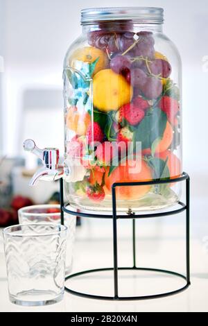 Nahansicht Glass Maurer Gallone Glas Getränkespender mit Ständer gefüllt mit frischen reifen mehrfarbigen Yummy Früchten und Beeren und leeren Gläsern Stockfoto