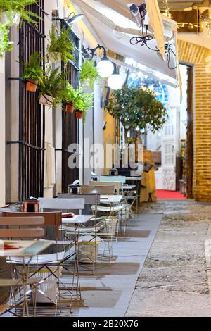 Charmantes Café mit Terrasse auf dem Bürgersteig, leeren Tischen und Stühlen aus Metall auf der Straße, die von Laternen beleuchtet wird, Nachtansicht der spanischen Stadt Sevilla. Spanien Stockfoto