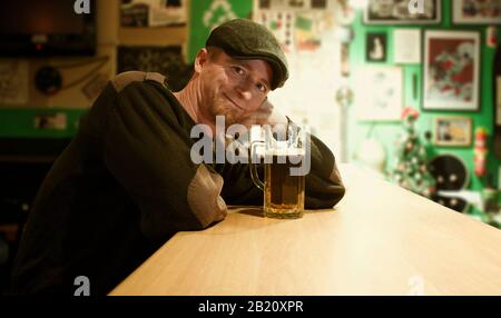 Der rothaarige, fast irischstämmige Kerl sitzt in der Bar und sieht sich an und trinkt ein paar Bier mit einem fröhlichen Gesicht Stockfoto
