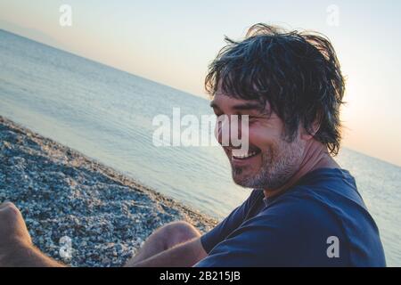 Ein gutaussehender Mann, der sich am Strand in Griechenland erholt, während er Sonnenuntergänge/Portrait eines gutaussehenden Mannes mittleren Alters zeigt Stockfoto