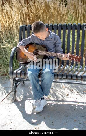 An einem schönen Herbsttag übt ein kleiner Junge seine akustische Gitarre im Freien aus Stockfoto