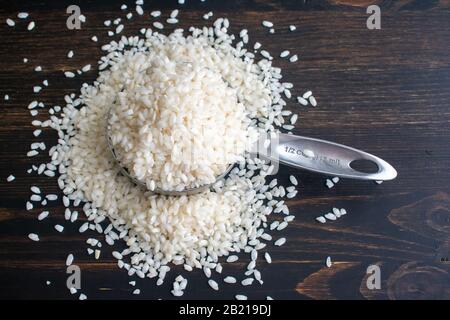 Arborio Rice in a Measuring Cup: Roher Kurzkornreis in einem Messbecher auf dunklem Holzhintergrund Stockfoto