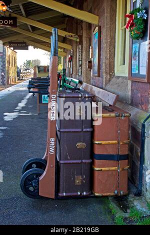 Gepäckhosen im alten Stil auf einem Rollwagen auf dem Bahnsteig am Bahnhof Dunster, West Somerset Railway, Dunster, Somerset, England Stockfoto