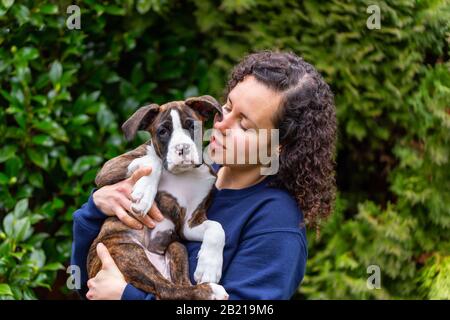 Weiße Kaukasianerin mit einem kleinen süßen Boxer Puppy draußen im Garten. Aufgenommen in Vancouver, British Columbia, Kanada. Stockfoto