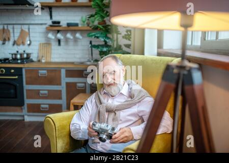 Senior sitzt im Sessel und hält eine Filmkamera Stockfoto