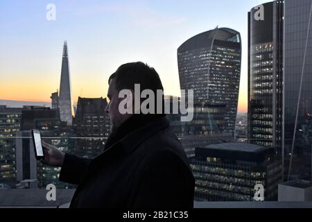Business man verwendet Smartphone draußen in der Winter City of London mit Bürohochhaus Wahrzeichen Gebäude Nacht Himmel & Shard Walkie Talkie auf Skyline UK Stockfoto