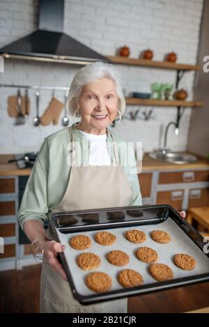 Lächelnde ältere Frau, die gerade gebackene Plätzchen hält Stockfoto