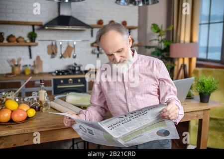 Konzentrierter älterer Mann, der Nachrichten in seiner Zeitung liest Stockfoto