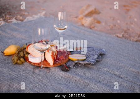 Holzbrett mit Brotbirnen-Feigen Nüsse grüne Trauben und köstlichen Käse mit zwei Gläsern Weißwein auf Decke Stockfoto