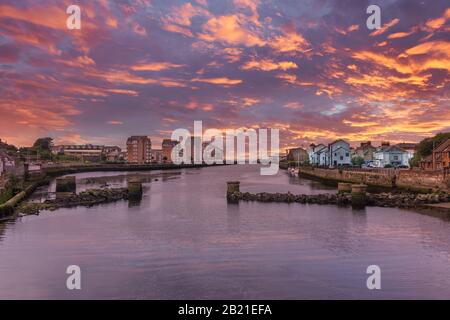 Von der neuen Brücke bei Ayr aus, die bei Sonnenuntergang über die zerstörten Fundamente und Säulen der alten Brücke in der historischen Stadt Ayr in Schottland blickt. Stockfoto