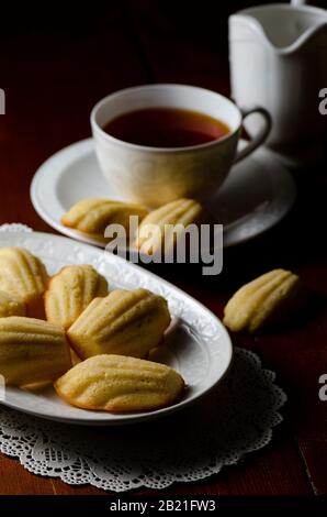 Traditionelle französische Madeleinen mit einer Tasse Tee auf dunklem Holzhintergrund Stockfoto