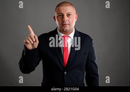 Porträt eines coolen Geschäftsmannes mit elegantem schwarzen Anzug und roter Krawatte, die keinen isolierten Hintergrund über grauem Hintergrund zeigen Stockfoto