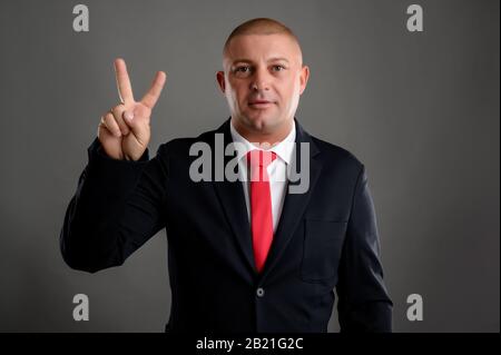 Porträt eines coolen Geschäftsmannes mit elegantem schwarzen Anzug und roter Krawatte, die zwei isolierte über grauem Hintergrund zeigen Stockfoto