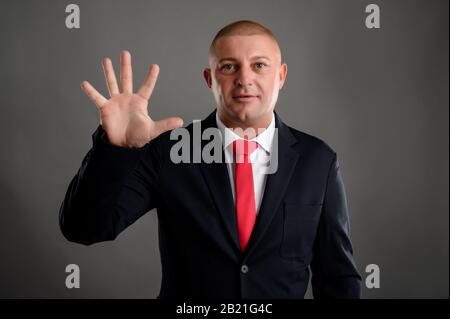 Porträt eines coolen Geschäftsmannes mit elegantem schwarzen Anzug und roter Krawatte, die fünf isoliert über grauem Hintergrund zeigen Stockfoto