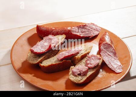 Sandwiches mit Crakow-Wurst auf braunem Teller und weißem Holztisch Stockfoto