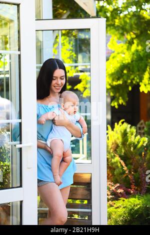 Junge schöne Mutter umarmte ihren kleinen Babysohn im Freien. Mutter und Baby haben zusammen Spaß im grünen Garten. Glückliche Familie, Kind und Elternschaft Stockfoto