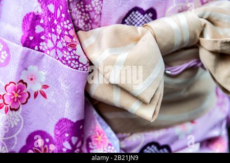 Kyoto, Japan Nahaufnahme der Frau in lila Kimono mit Kirschblütenmuster, pinkfarbenem Federmuster und gebundenem Schleife obi-Gürtel Stockfoto