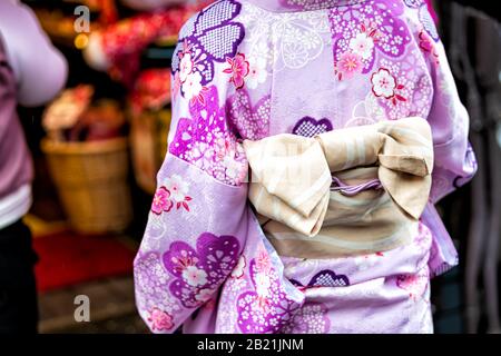 Kyoto, Japan Nahaufnahme der nicht erkennbaren Frau in violettem Kimono mit Kirschblütenmuster, pinkfarbenem Federmuster und gebundenem Schleife obi-Gürtel Stockfoto