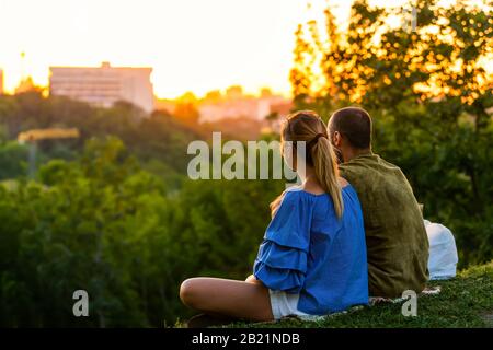 Kiew, Ukraine - 10. August 2018: Landschaftsallee in der Kiewer Hauptstadt mit Paar Blick auf den Sonnenuntergang goldenes Sonnenlicht sitzend mit Picknick Stockfoto