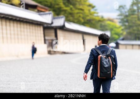 Kyoto, Japan - 17. April 2019: Mann mit Rucksacksalaryman, der auf der Straße der Stadt durch die Mauer läuft, Außeneingang des kaiserlichen Palastes Stockfoto