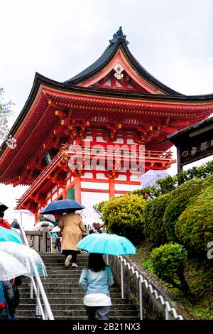 Kyoto, Japan - 9. April 2019: Viele Menschen mit Sonnenschirmen, die an regnerischen Tagen auf einer Straßentreppe hinauf in Richtung der roten Pagode des Kiyomizu-dera-Tempels gehen Stockfoto