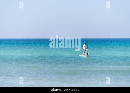 Santa Rosa Beach, USA - 25. April 2018: Mann auf Stehbrett mit Angelruten paddeln im altantischen Ozean am Horizont in Pensacola Stockfoto