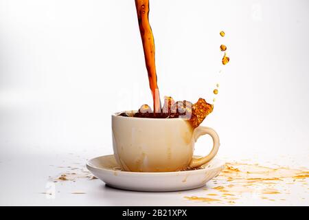Kaffee, der in eine weiße Tasse eingießt, isoliert vor einem einfarbigen weißen Hintergrund, spritzt in alle Richtungen und erzeugt so ein Durcheinander auf der weißen Oberfläche Stockfoto