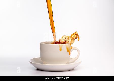 Kaffee, der in eine weiße Tasse eingießt, isoliert vor einem einfarbigen weißen Hintergrund, spritzt in alle Richtungen und erzeugt so ein Durcheinander auf der weißen Oberfläche Stockfoto