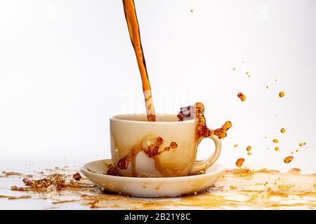Kaffee, der in eine weiße Tasse eingießt, isoliert vor einem einfarbigen weißen Hintergrund, spritzt in alle Richtungen und erzeugt so ein Durcheinander auf der weißen Oberfläche Stockfoto