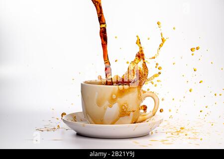 Kaffee, der in eine weiße Tasse eingießt, isoliert vor einem einfarbigen weißen Hintergrund, spritzt in alle Richtungen und erzeugt so ein Durcheinander auf der weißen Oberfläche Stockfoto