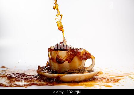 Kaffee, der in eine weiße Tasse eingießt, isoliert vor einem einfarbigen weißen Hintergrund, spritzt in alle Richtungen und erzeugt so ein Durcheinander auf der weißen Oberfläche Stockfoto