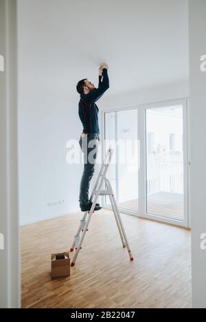 Hausbesitzer steht auf der Leiter, um die Lichtinstallation zu befestigen Stockfoto